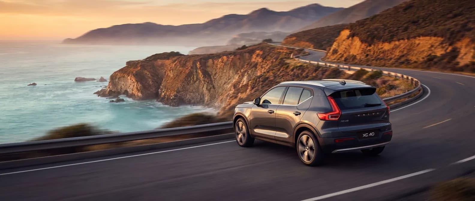 Volvo XC40 B3 roulant sur une route côtière panoramique au coucher du soleil, soulignant son design élégant et sa puissance.