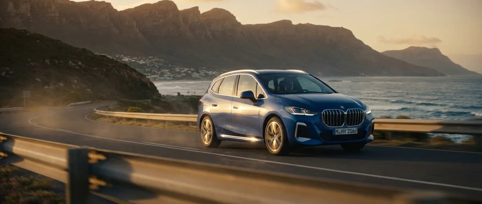 BMW 216d Active Tourer roulant sur une route côtière au coucher du soleil