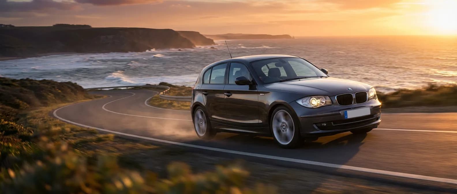 La BMW 130d : Puissance et Aventure sur la Côte BMW 130d (E87) sur une route côtière au coucher du soleil, puissance et élégance.