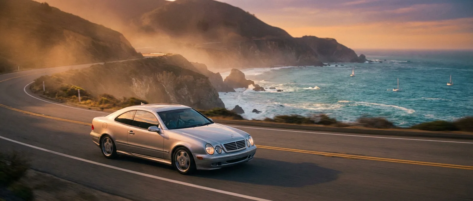 Une Mercedes CLK W208 argentée roule sur une route côtière au coucher du soleil.