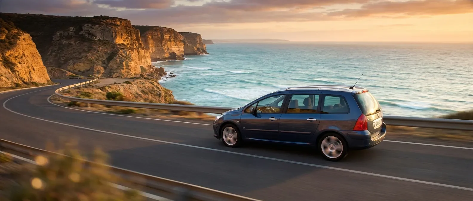 Peugeot 307 SW en mouvement sur une route côtière au lever du soleil, mettant en valeur ses dimensions élégantes et son design.
